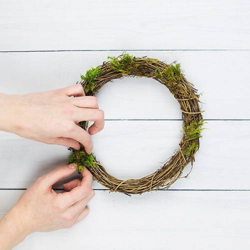 Person attaching moss to the wooden frame whilst placed against a white wooden background.