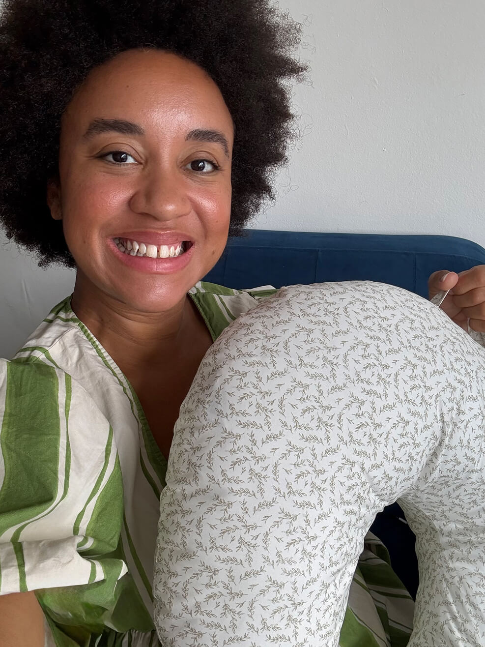 Smiling person holding a patterned pillow while sitting on a couch.