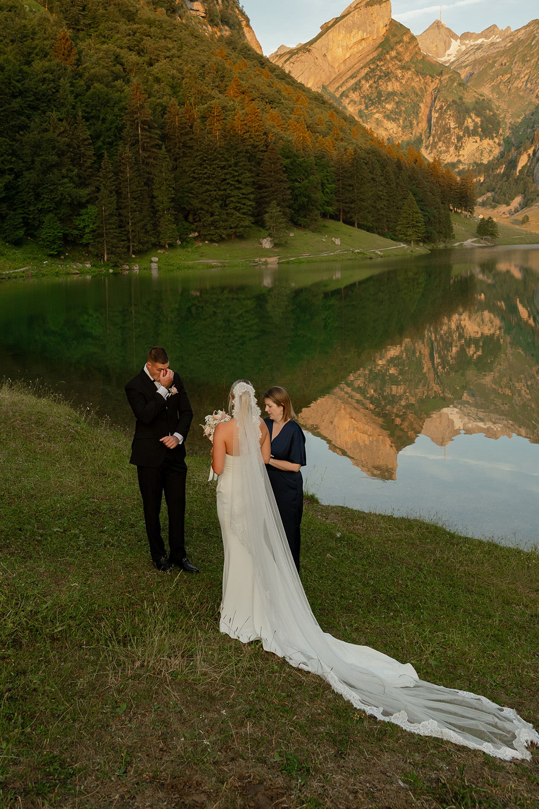 Bride and groom by a lake, surrounded by mountains and greenery.