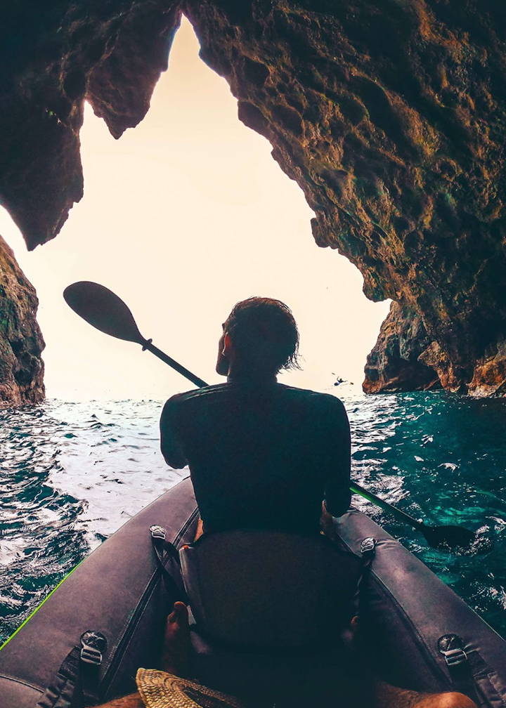 A photo of the backside of a man, paddling through the ocean inside of a sea cave.