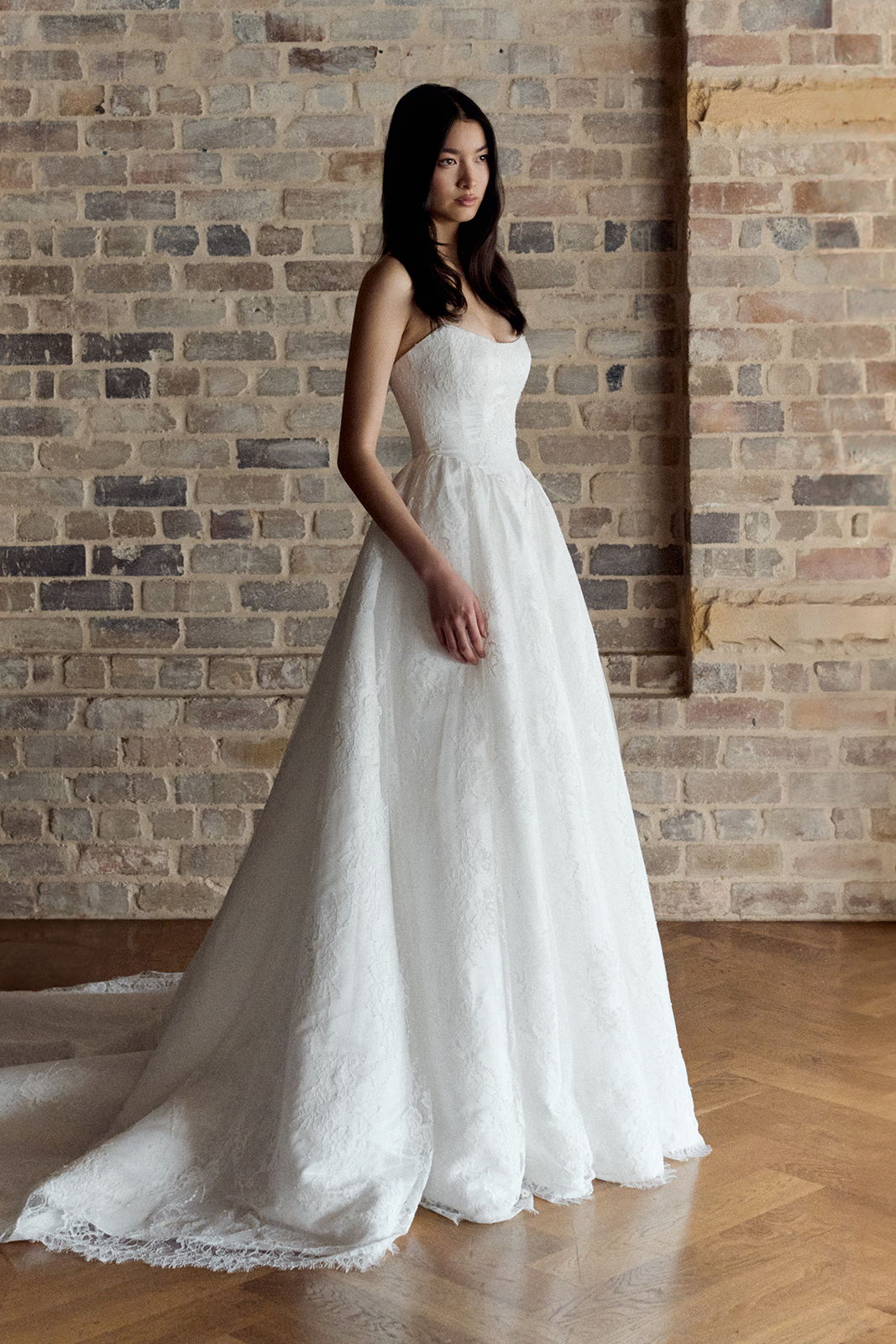 A model in a white wedding dress poses against a brick wall.