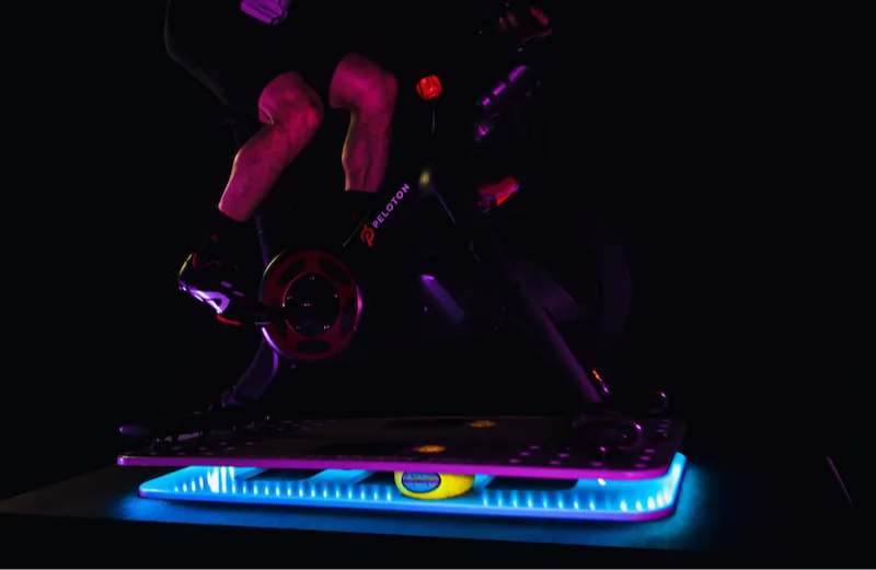 A cyclist riding a Peloton bike on the Velocity Rocker Spin with LED lights.