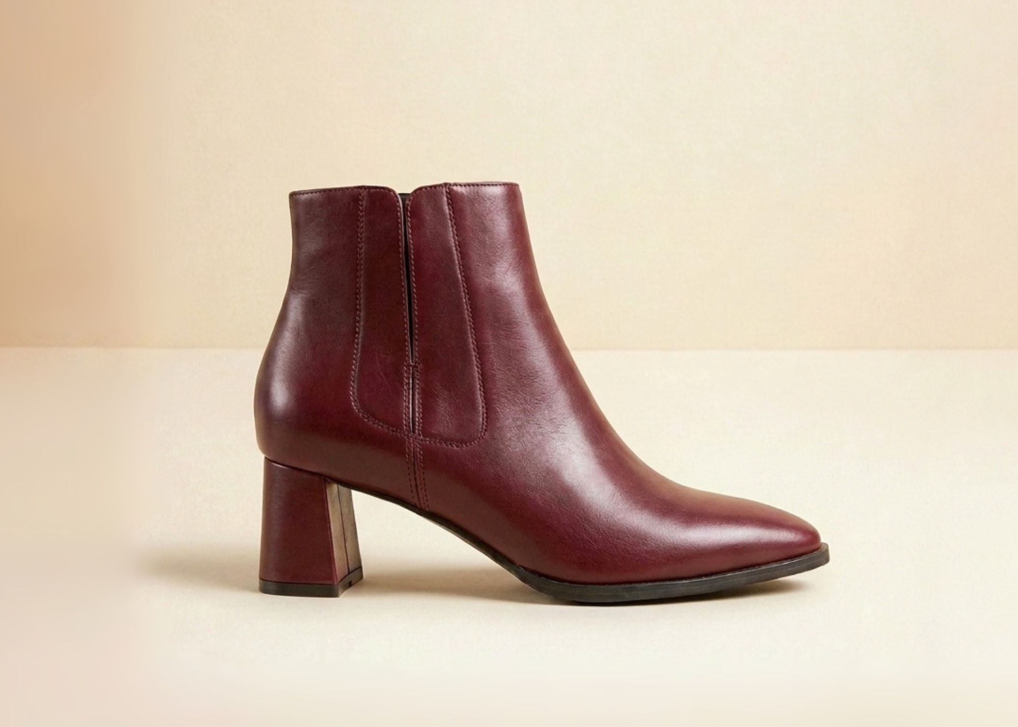 Burgundy leather ankle boots with a block heel on a neutral background.