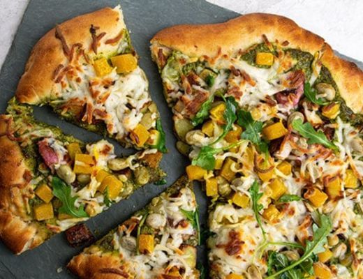 Pizza with vegetables and cheese, sliced on a gray surface.