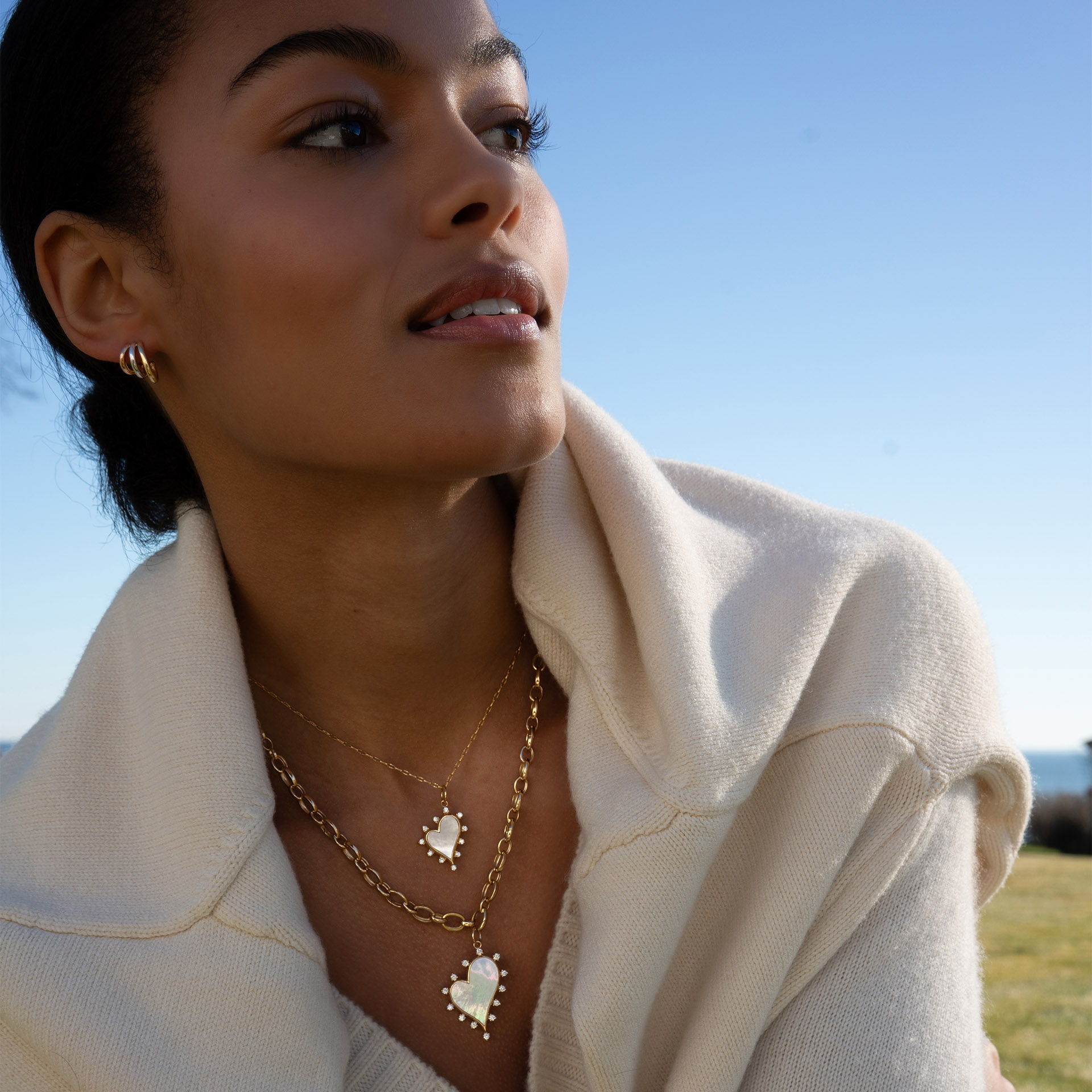 Woman wearing layered necklaces, looking thoughtfully into the distance on a sunny day.