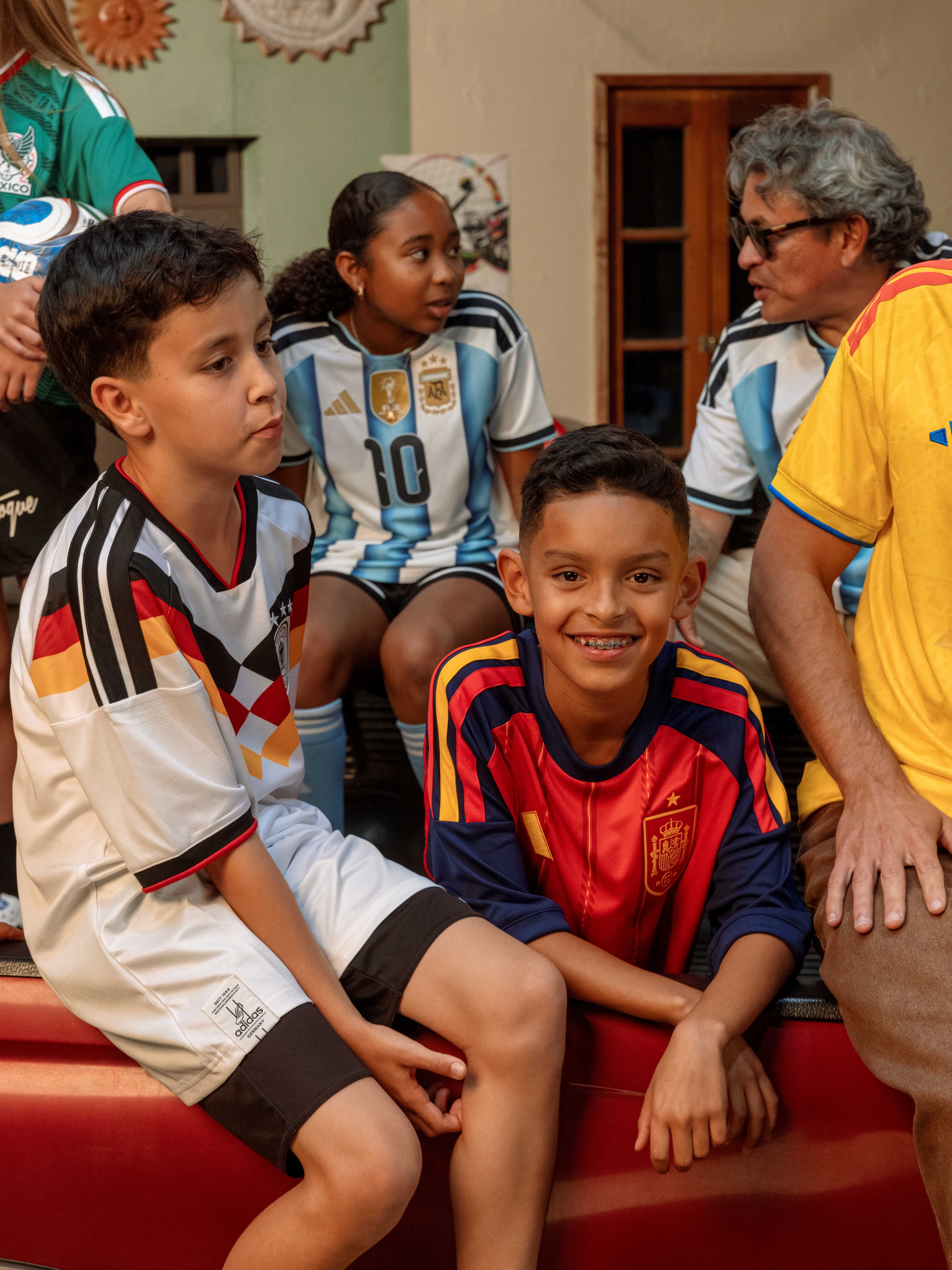 Children in soccer jerseys sitting together, smiling and engaged in conversation.