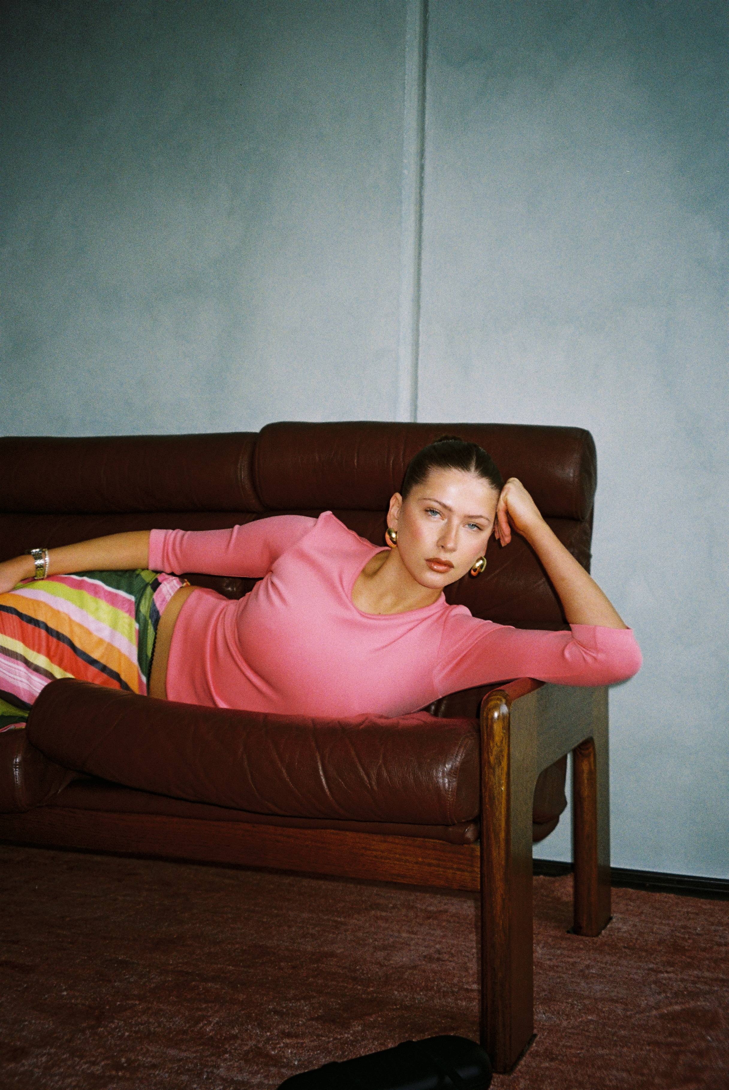 Woman in a pink top lounging on a brown sofa with colorful striped pants.