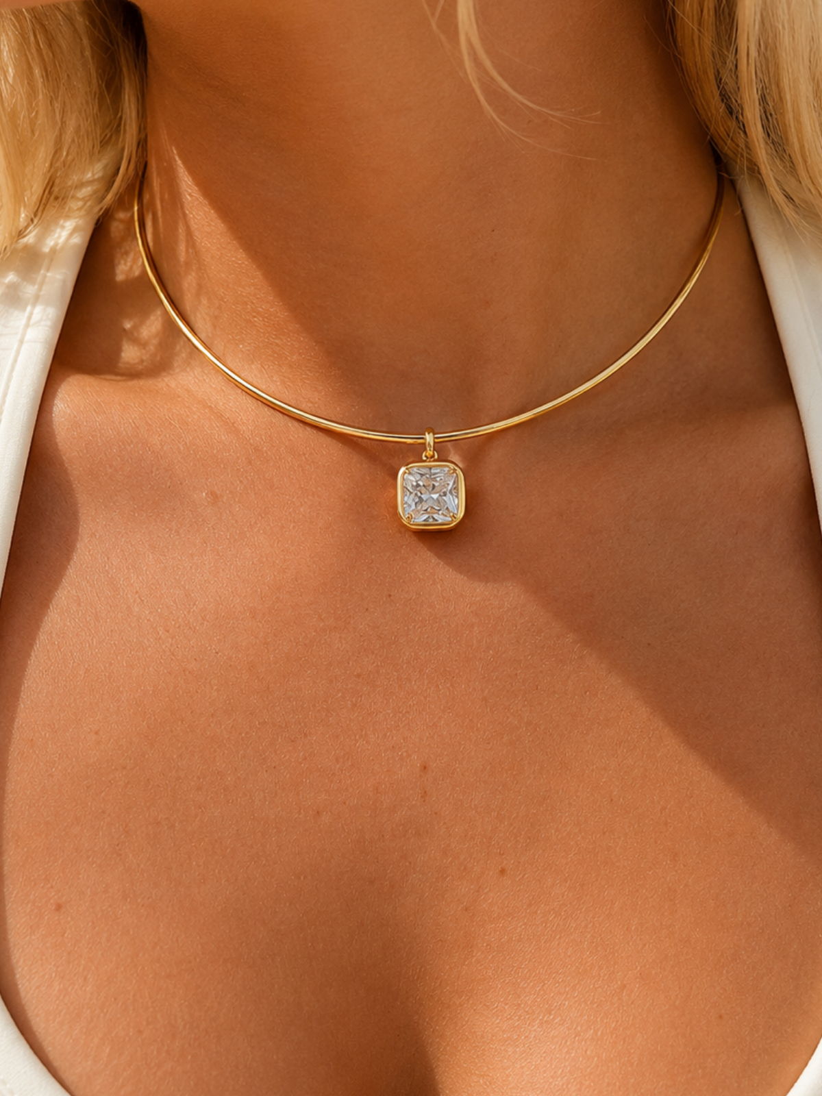 Model wearing a gold collar necklace with a bezel-set crystal pendant.