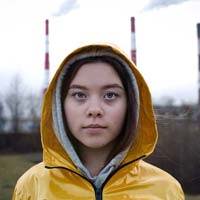 A young woman in a yellow rain jacket with a factory in the background