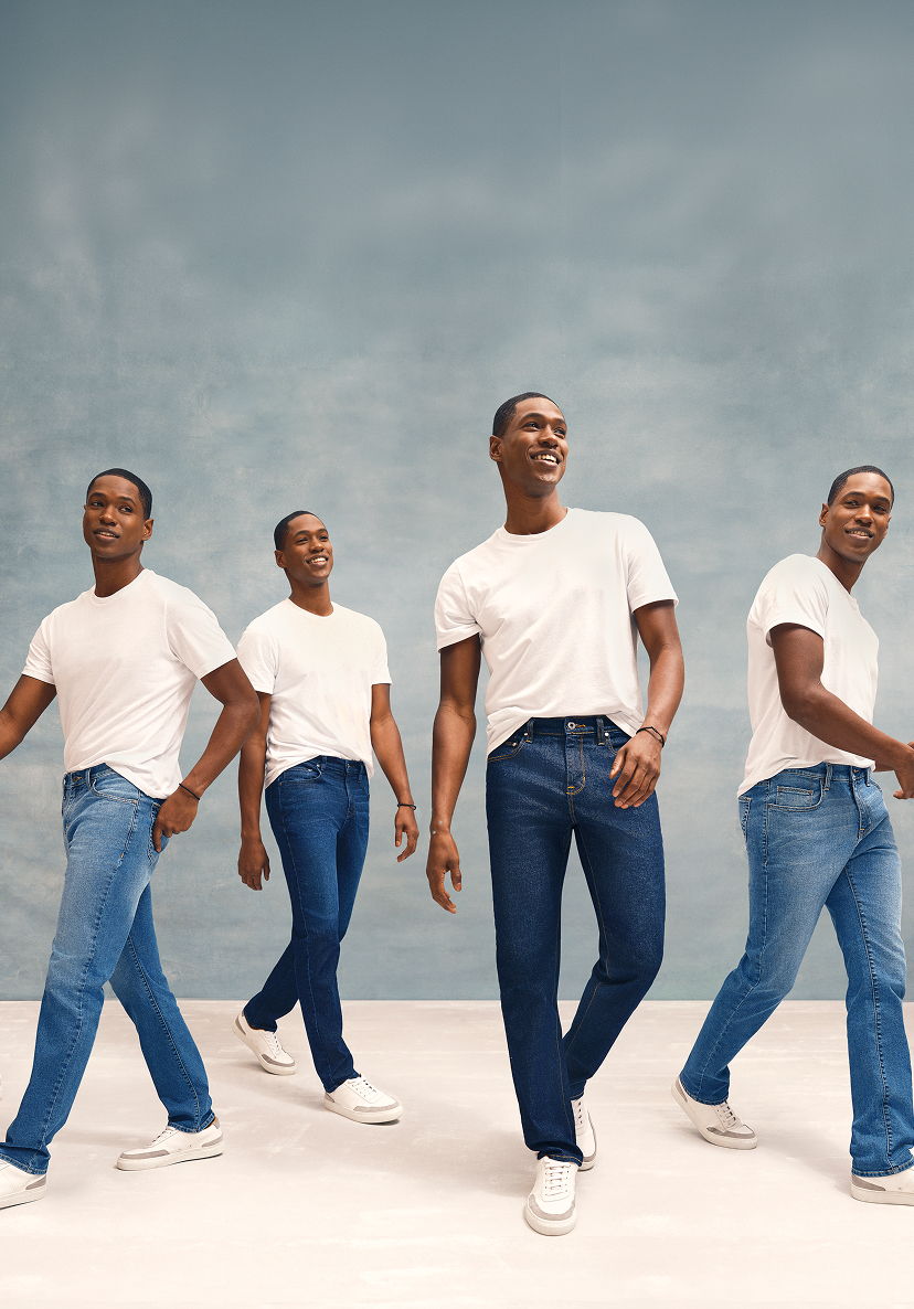 Four men in white t-shirts and jeans walking against a blue background.