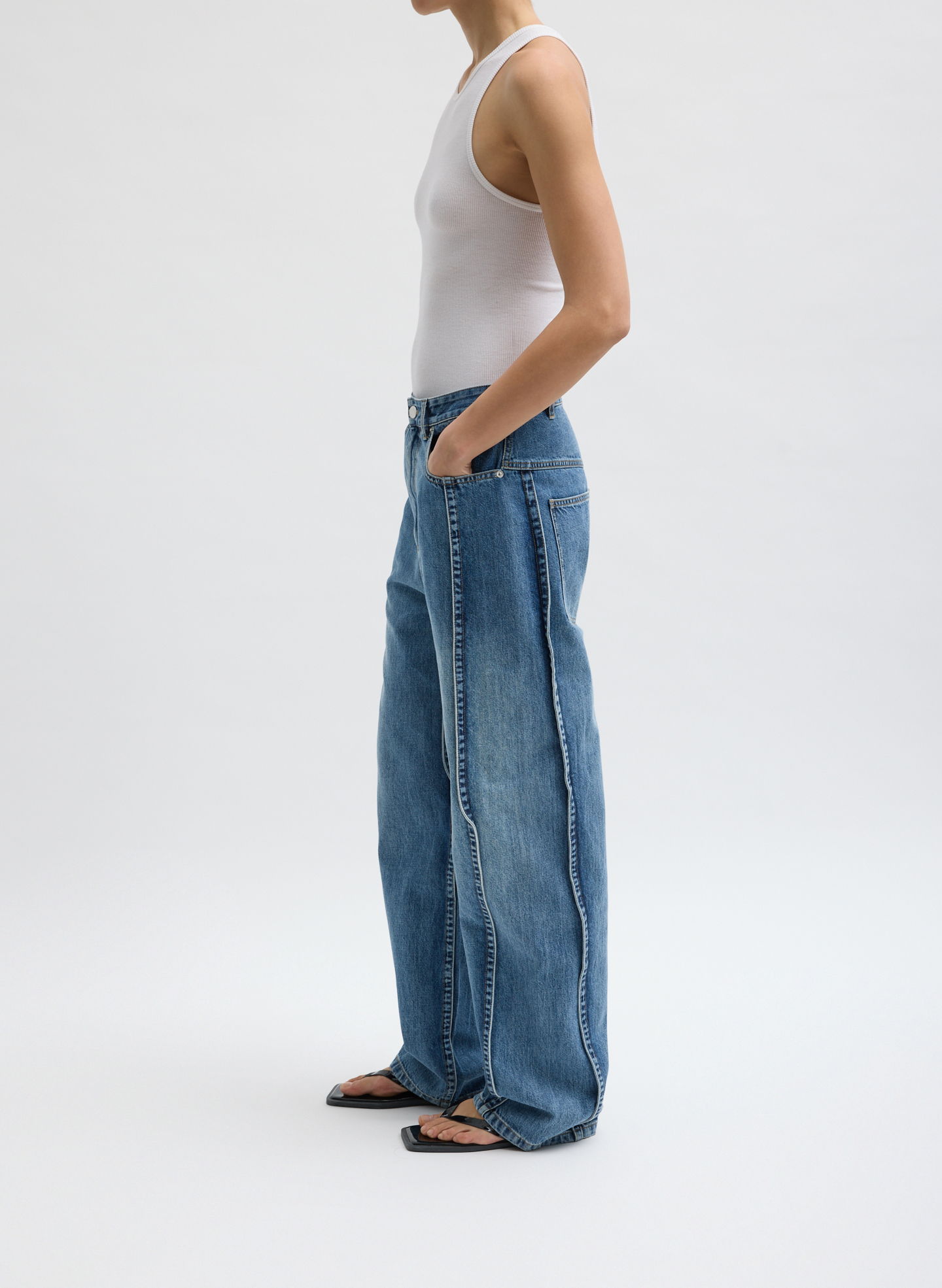 Person wearing a tank top and wide-leg jeans, standing sideways.
