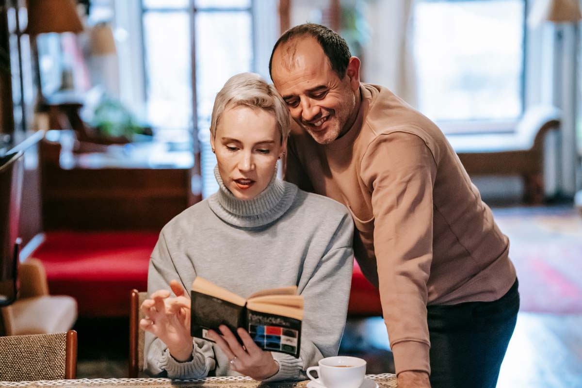 A mid-aged couple looking over a book together while drinking coffee