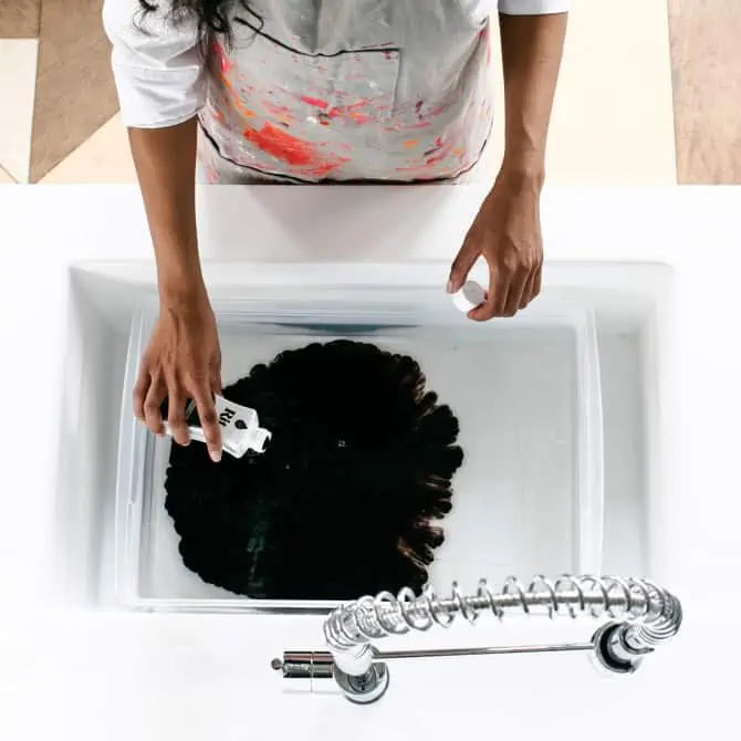 Person washing a large black paint or dye in a sink.