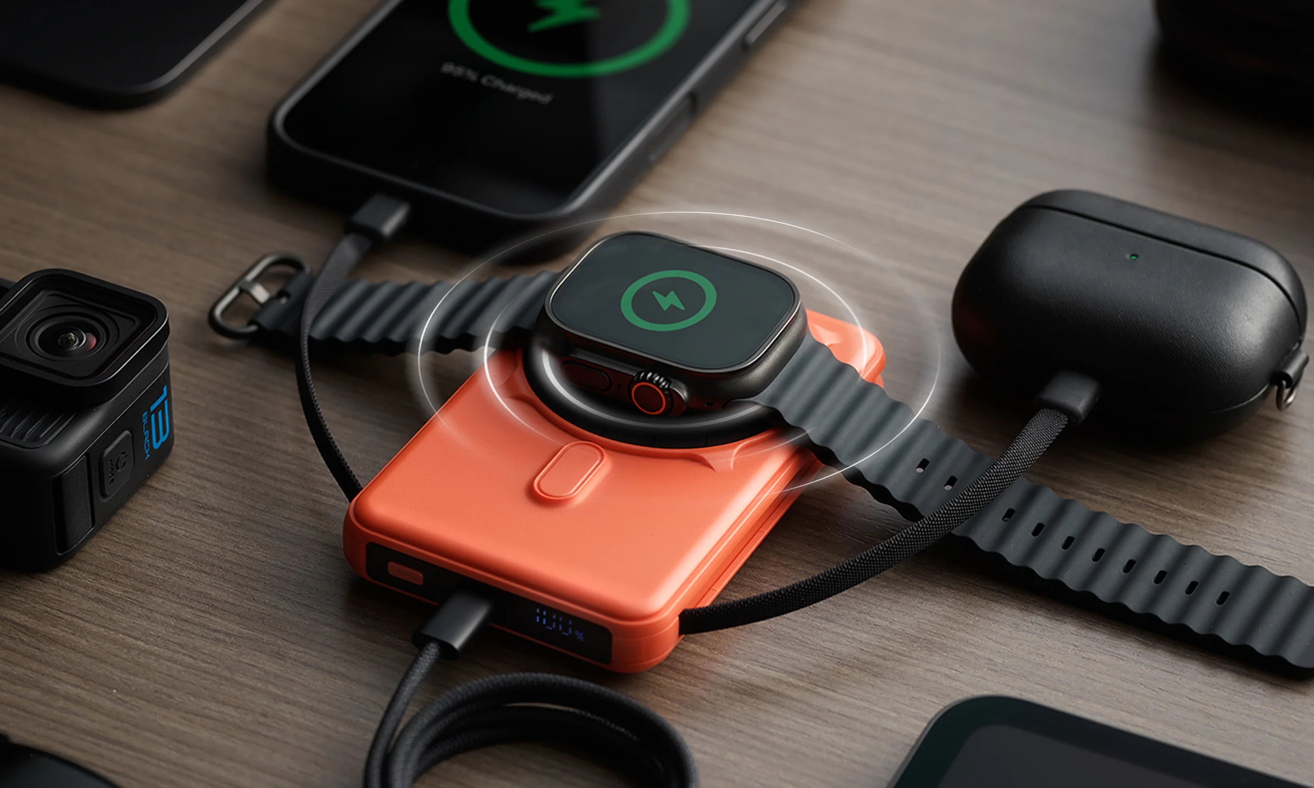 Smartwatch charging on an orange power bank among various electronic devices.