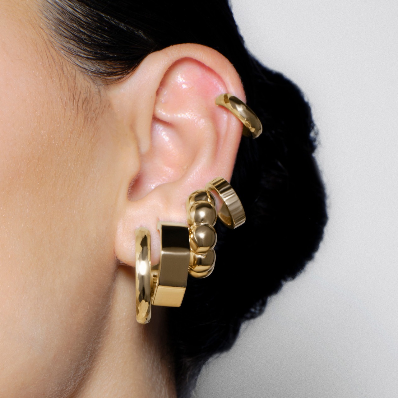 Close-up of a woman's ear adorned with multiple gold earrings.