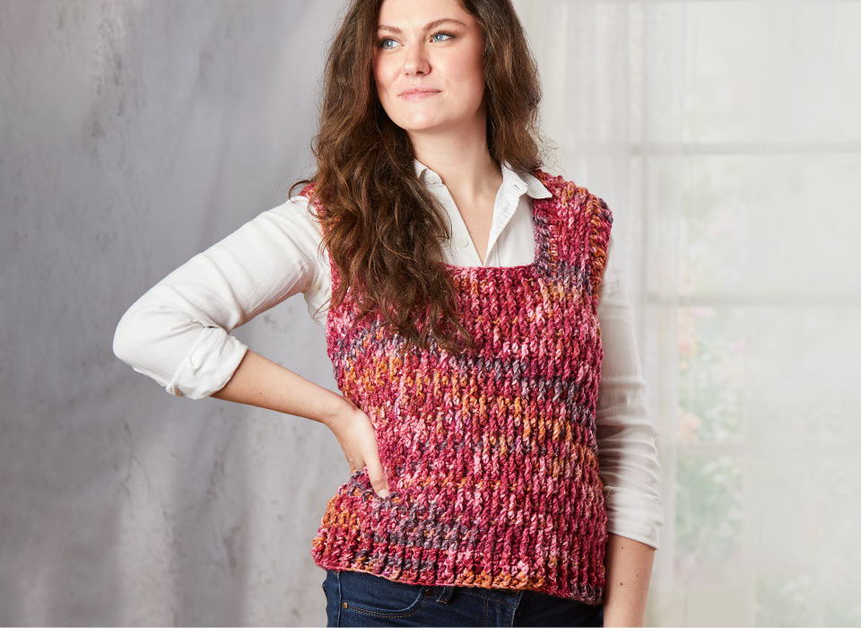 Woman wearing a colorful knitted vest over a white shirt, posing confidently.