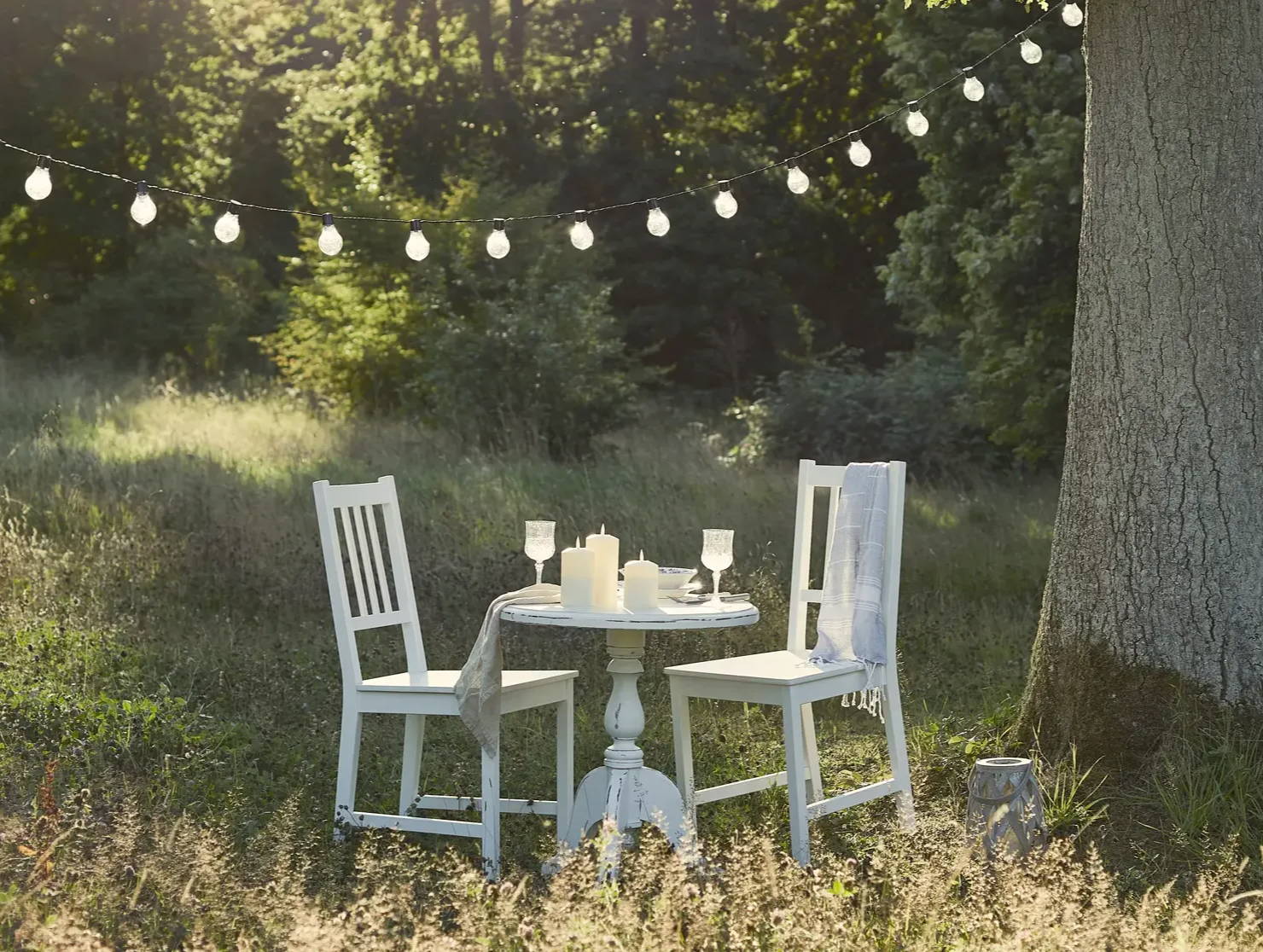 Meadow dining with festoons hung between trees and outdoor candles displayed on table