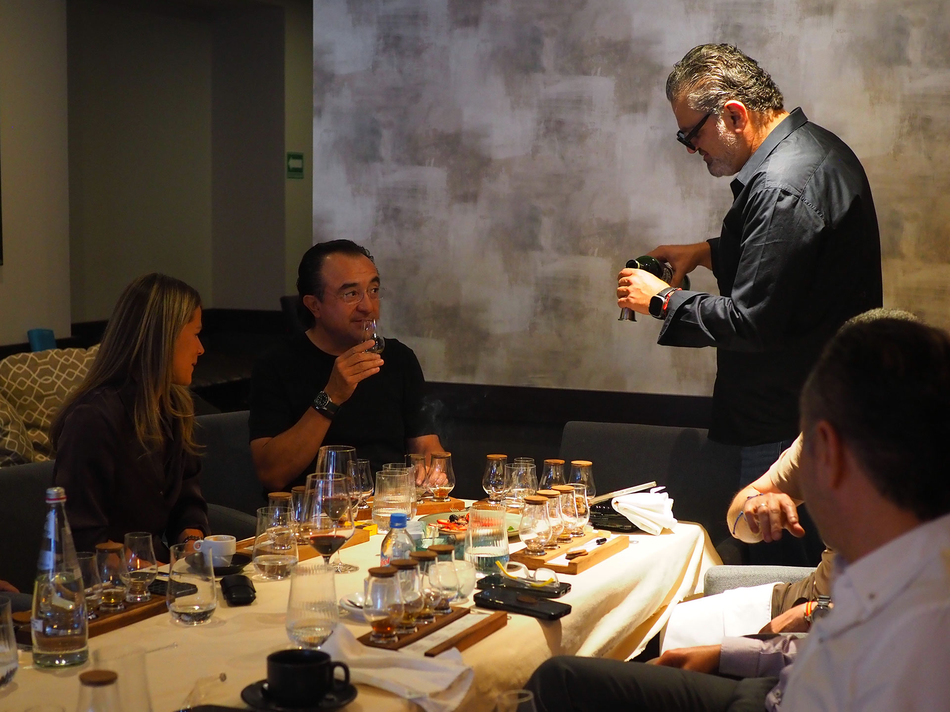 Group of people engaged in conversation around a table with food and drinks.