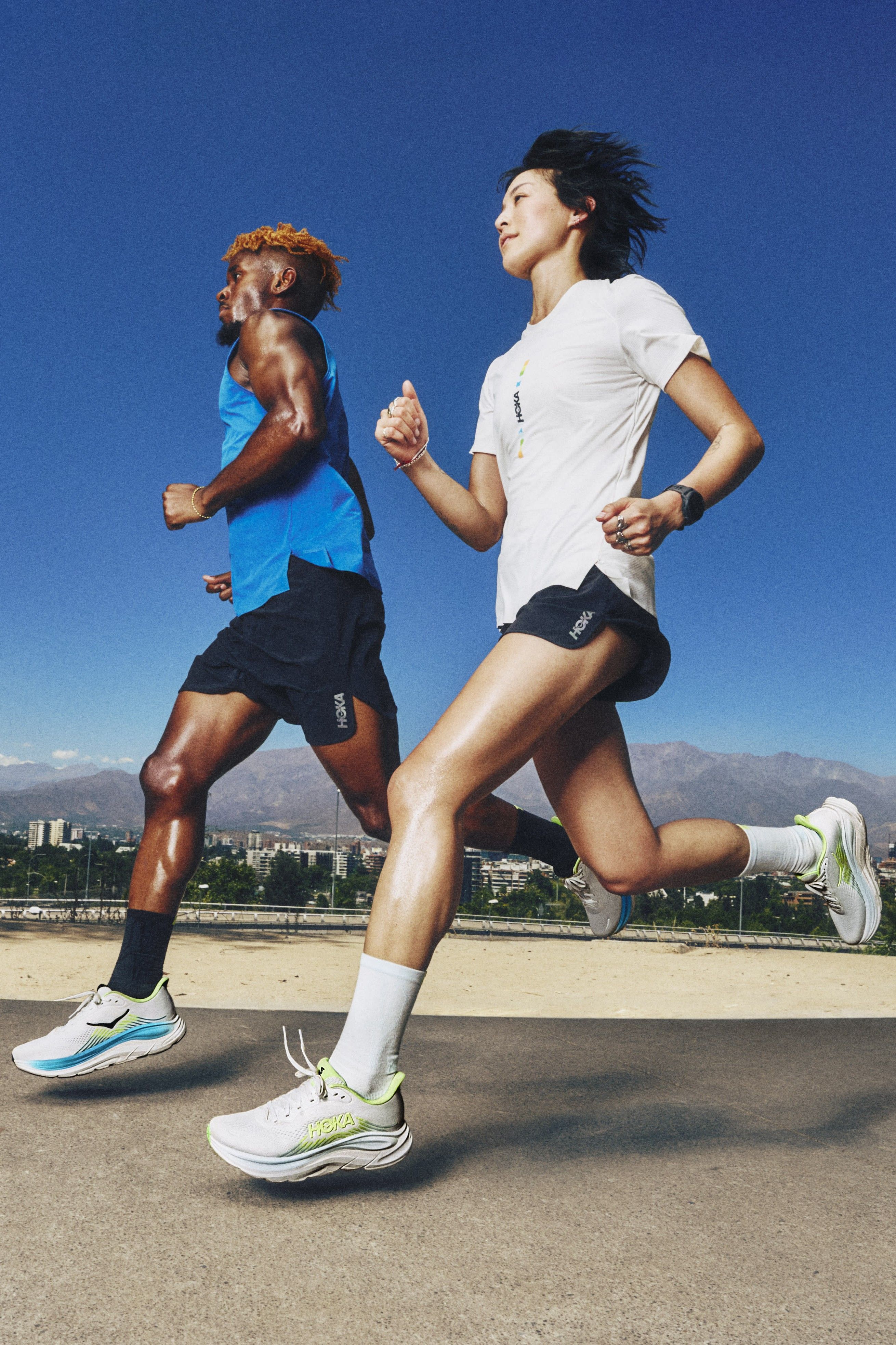 Two runners in athletic gear running outdoors against a blue sky.
