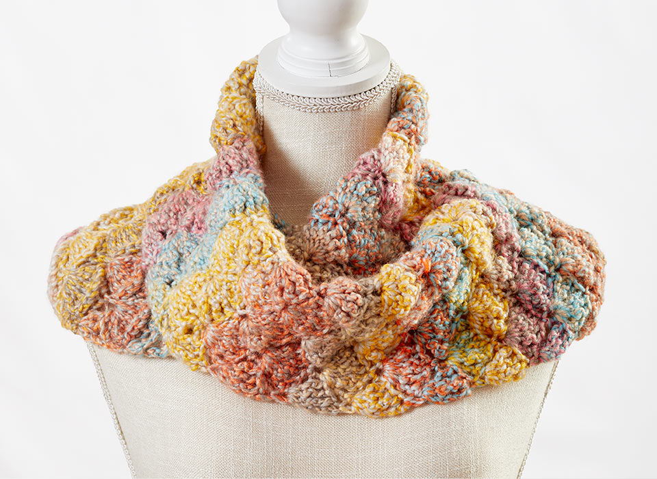 Colorful knitted infinity scarf displayed on a dress form.