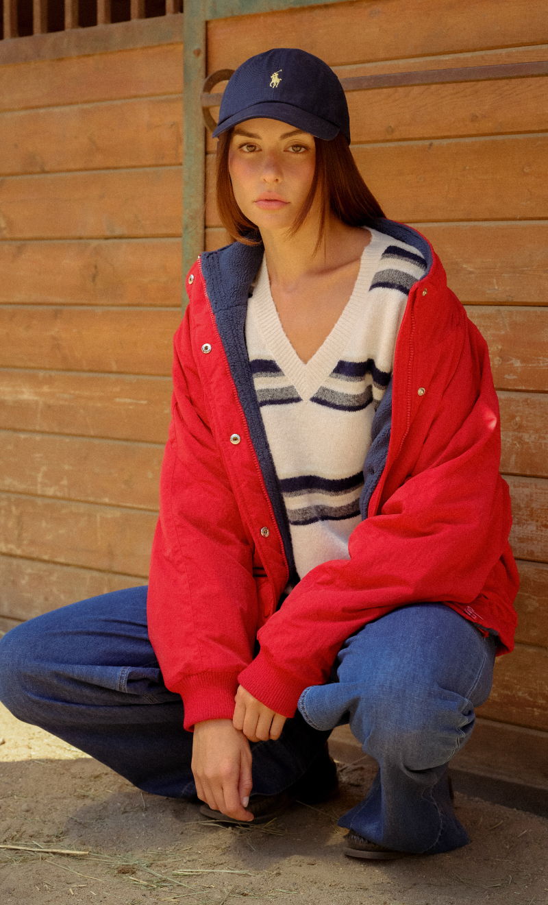 A person squatting in casual clothing near a wooden backdrop.
