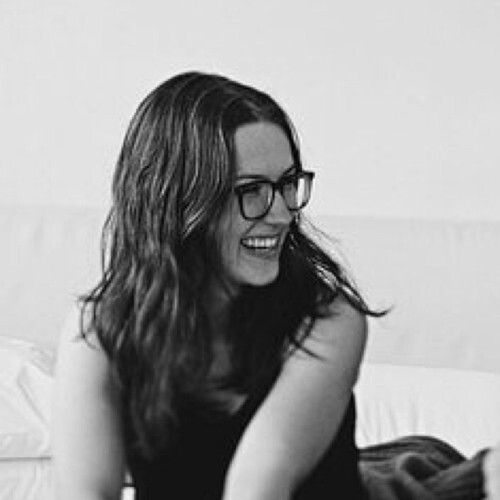 A woman with glasses smiling and sitting on a couch.
