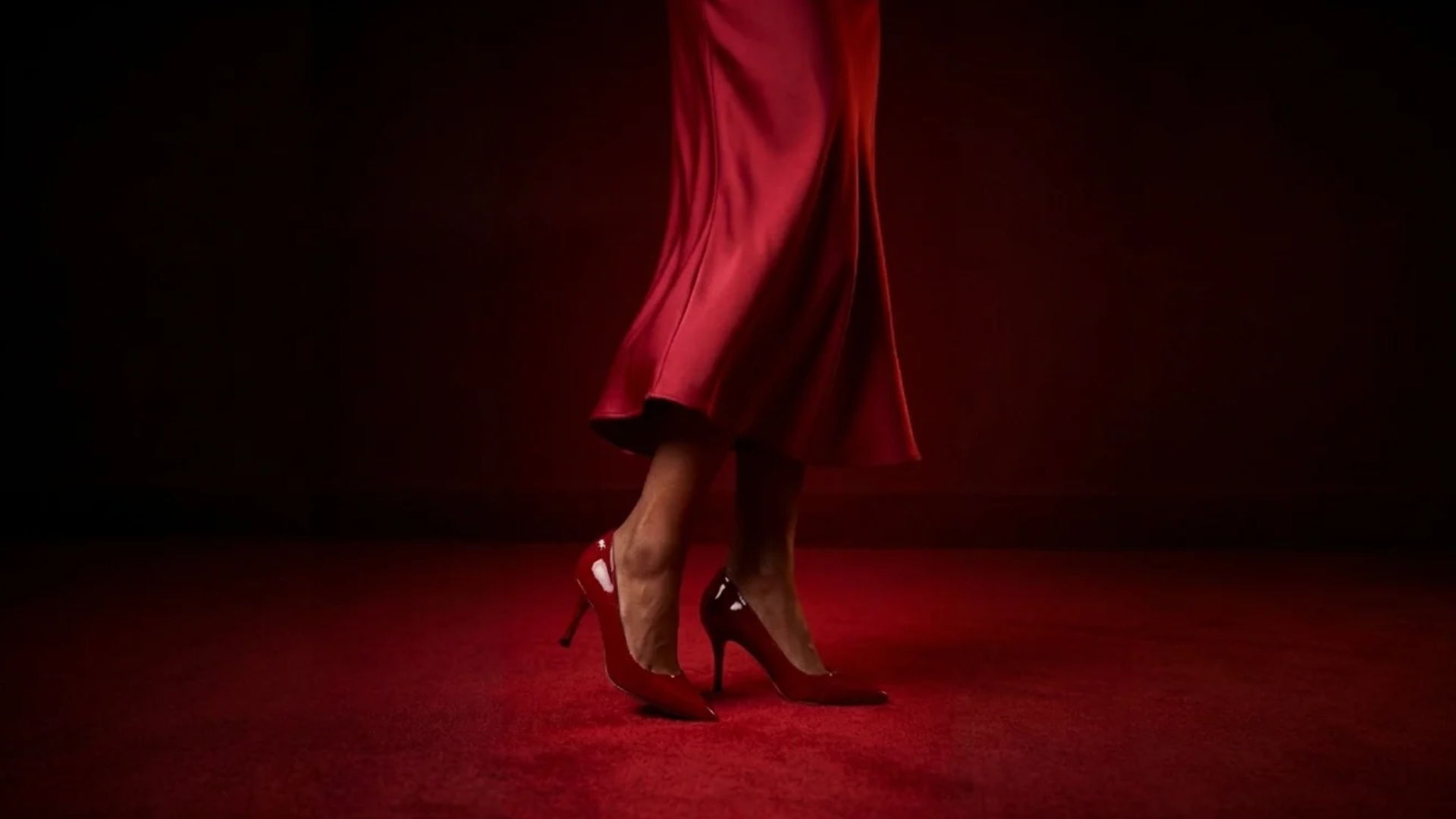 A woman's legs in a red dress and high heels on a red floor.