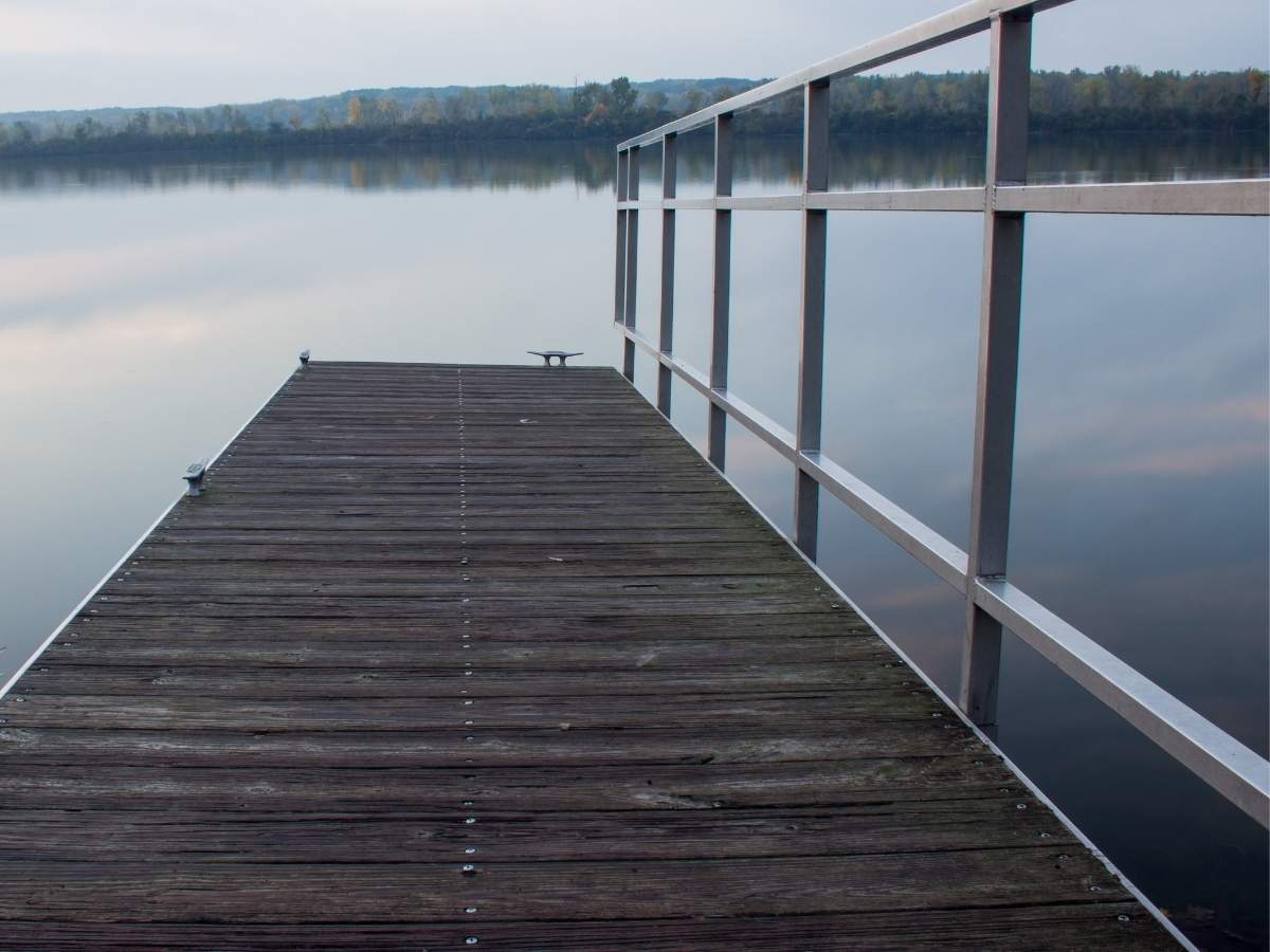 Wooden dock with square tubing handrails extending over calm water