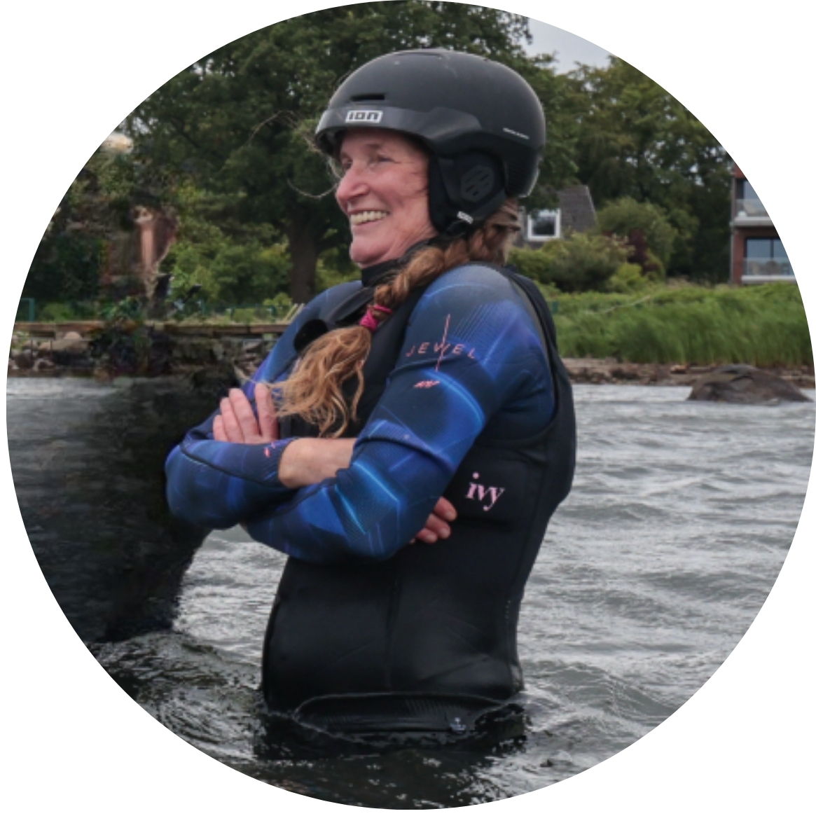 Smiling woman in wetsuit and helmet, standing in water.