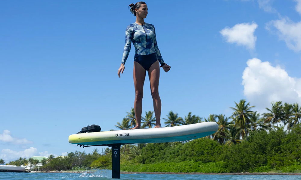 Une personne debout sur une planche de surf au-dessus de l'eau, avec des palmiers en arrière-plan.