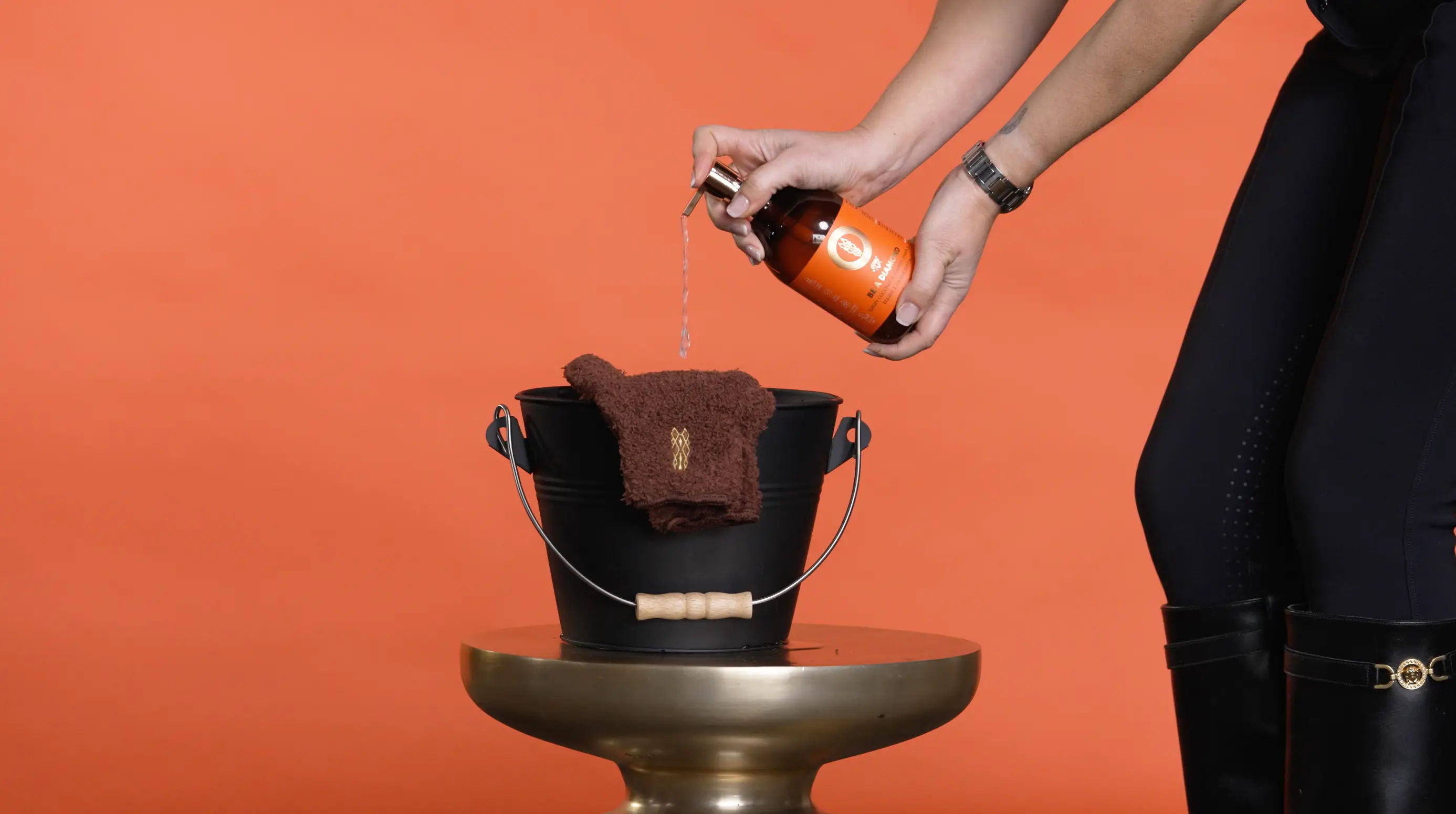 Person pouring Be A Diamond Shampoo into a black bucket on a gold table.