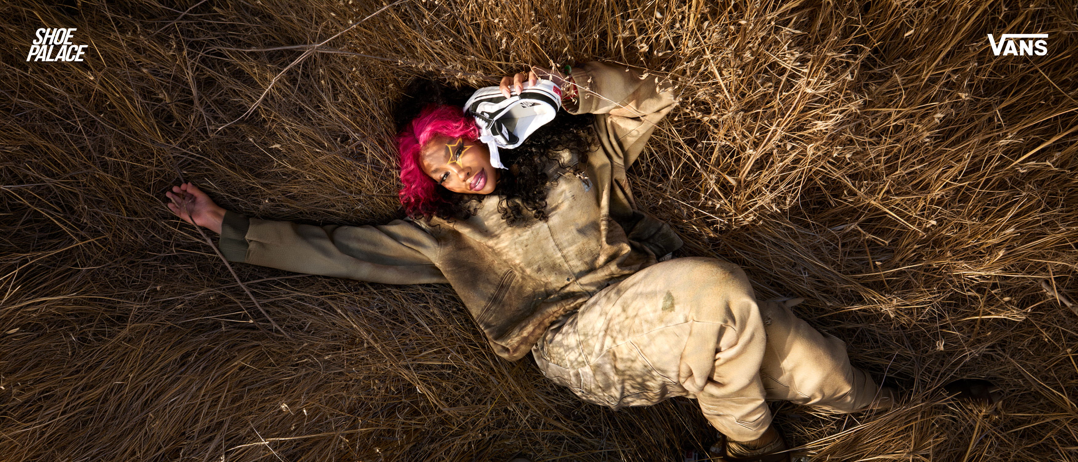 Person lying in grass, wearing a patterned outfit and holding a mask.
