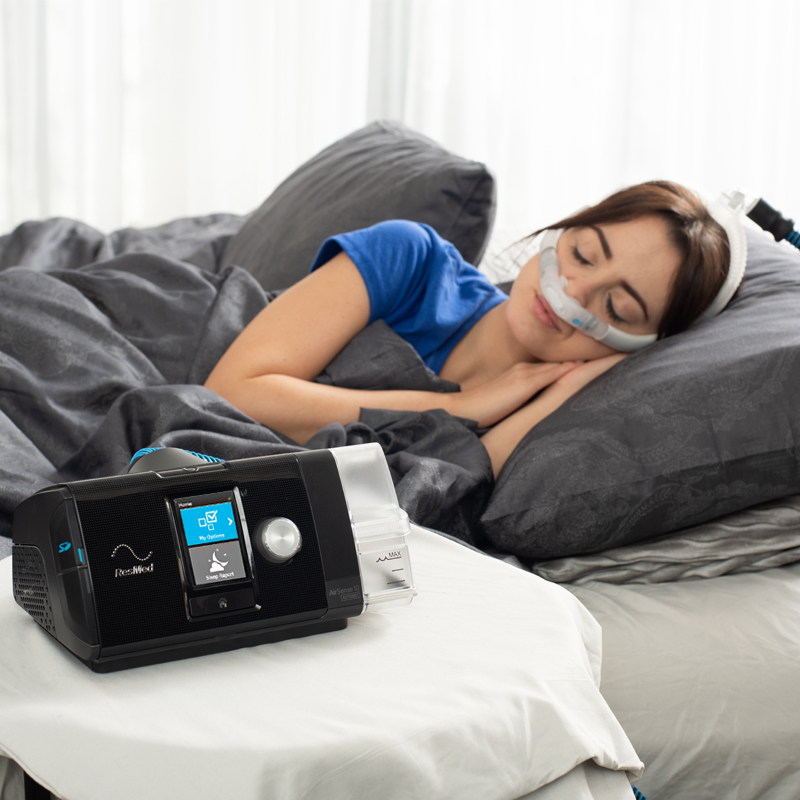 Woman sleeping with a CPAP machine beside her in a cozy bedroom.