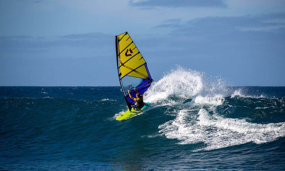 Une personne faisant de la planche à voile sur les vagues de l'océan, avec une voile Duotone et une planche de windsurf Duotone Grip SLS 2026.