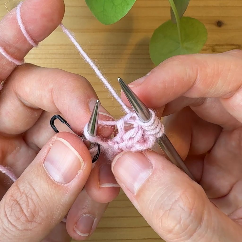 Rechtsgeneigte Zunahme stricken. Schritt 1.: Gehe mit deiner Linken Nadel von hinten unter dem Querfaden durch.