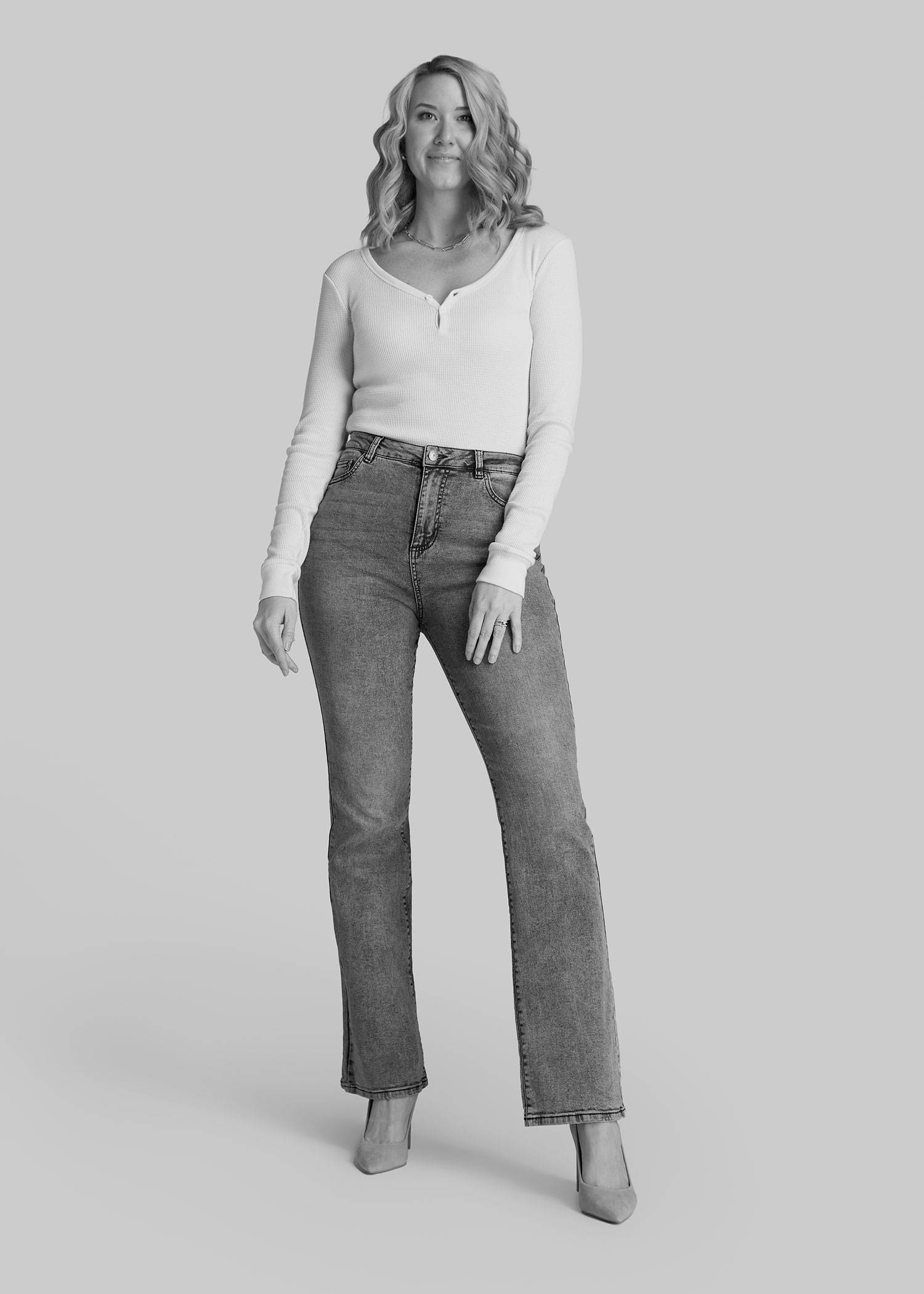 A tall woman wearing a white henley long sleeve and bootcut jeans