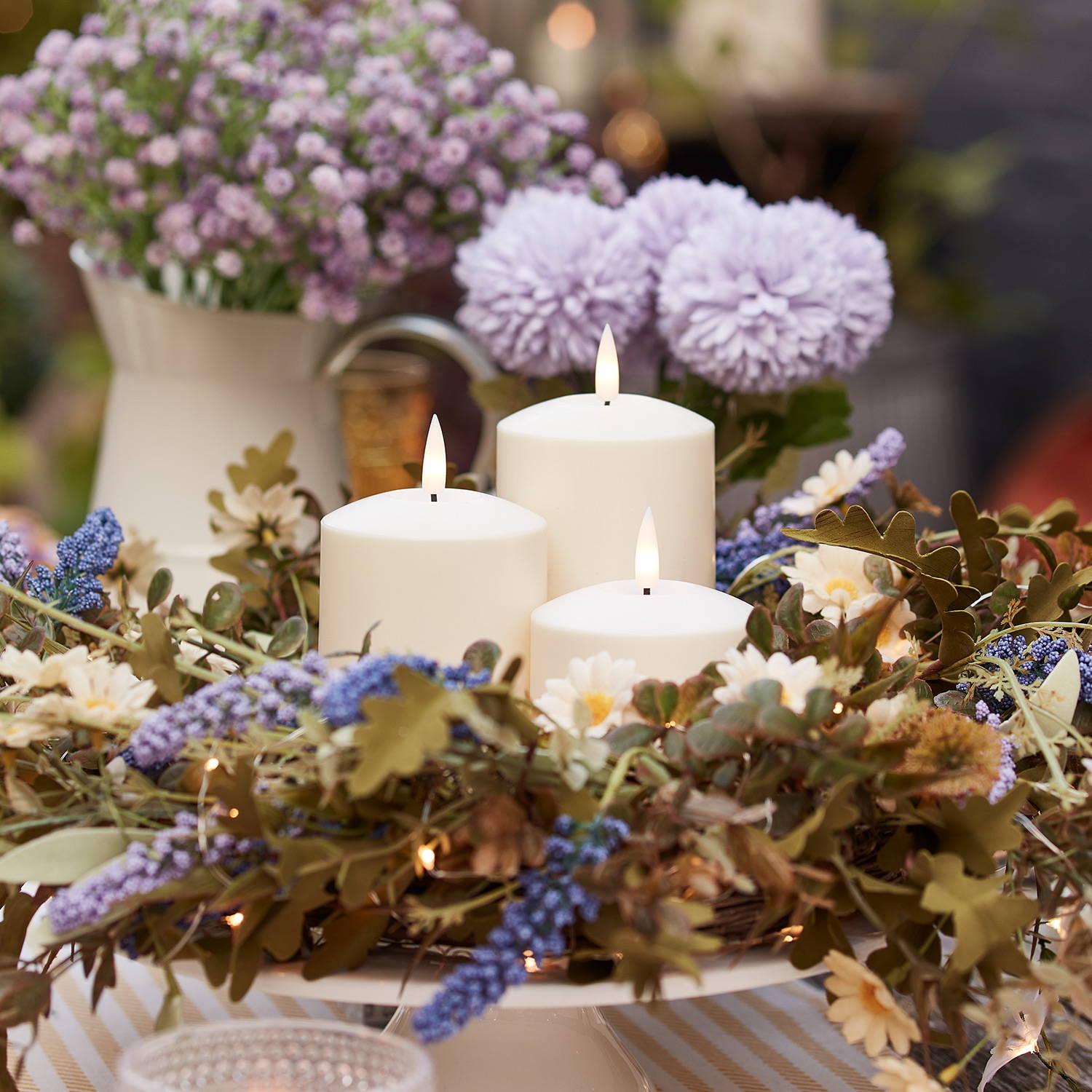 3 ivory LED pillar candles in the centre of a flower wreath as a dining table centrepiece.