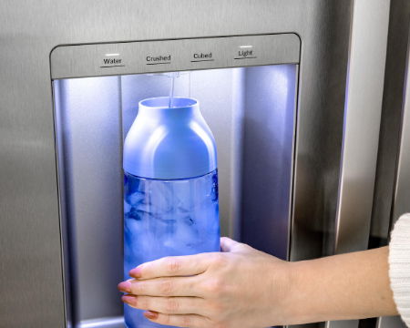 Hand placing a blue bottle in a refrigerator water dispenser.