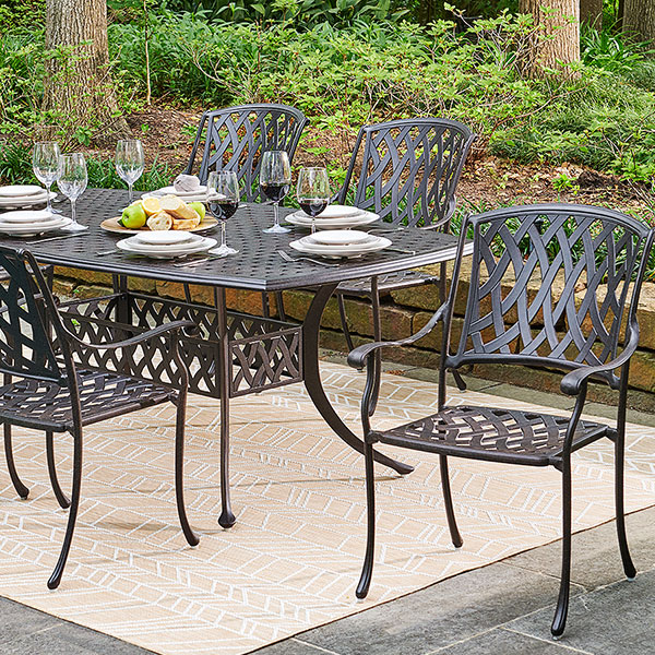 Outdoor dining table set with plates, glasses, and chairs in a garden.