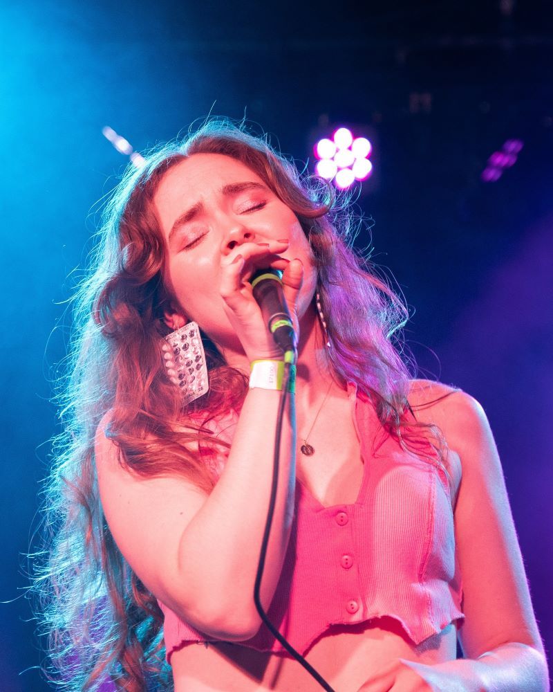 Singer performing on stage with a microphone, colorful lights in the background.