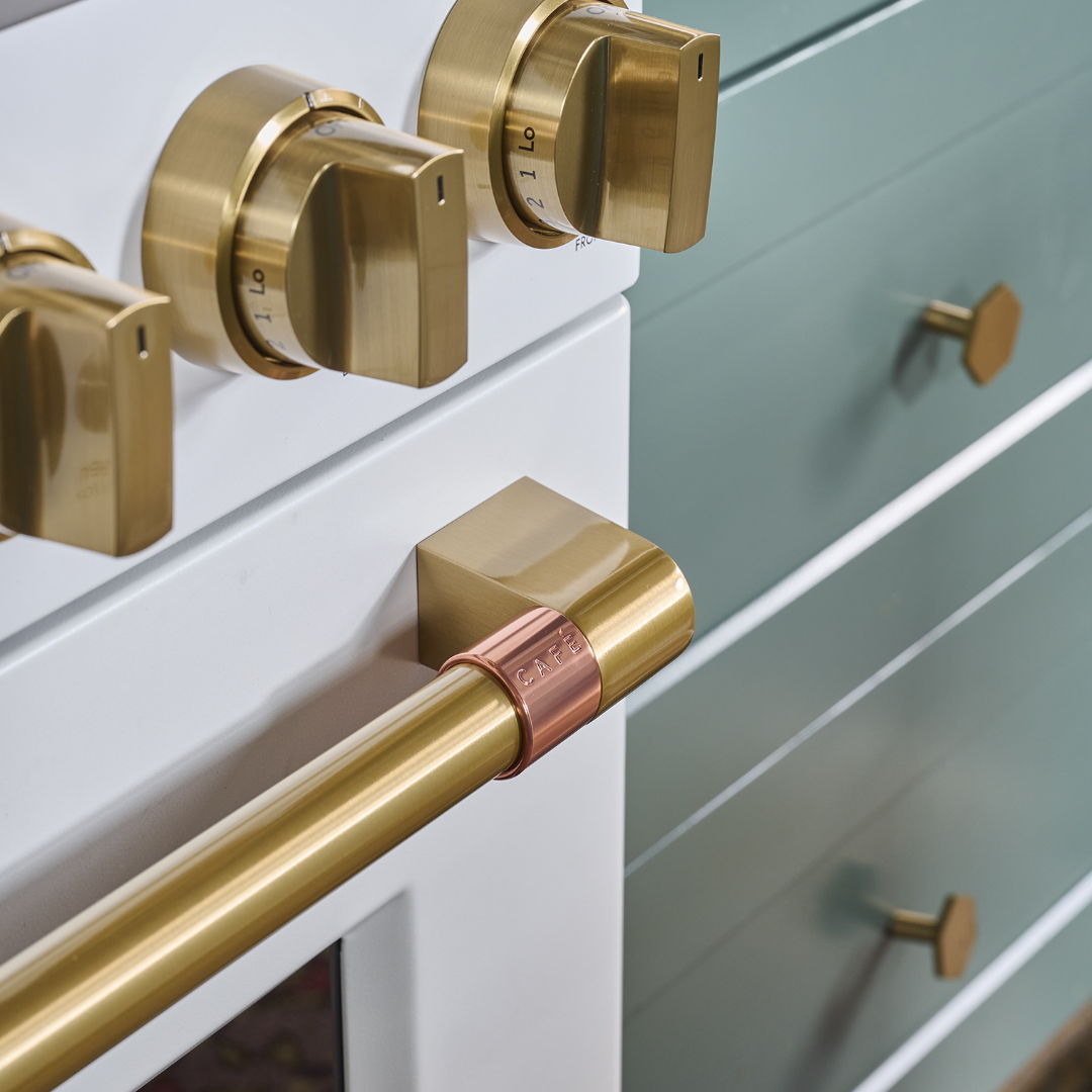 Brushed brass knobs and handles on a matte white range.