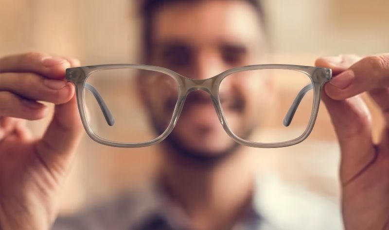 Man putting on Marvel Grey prescription eyeglasses with blurred background 