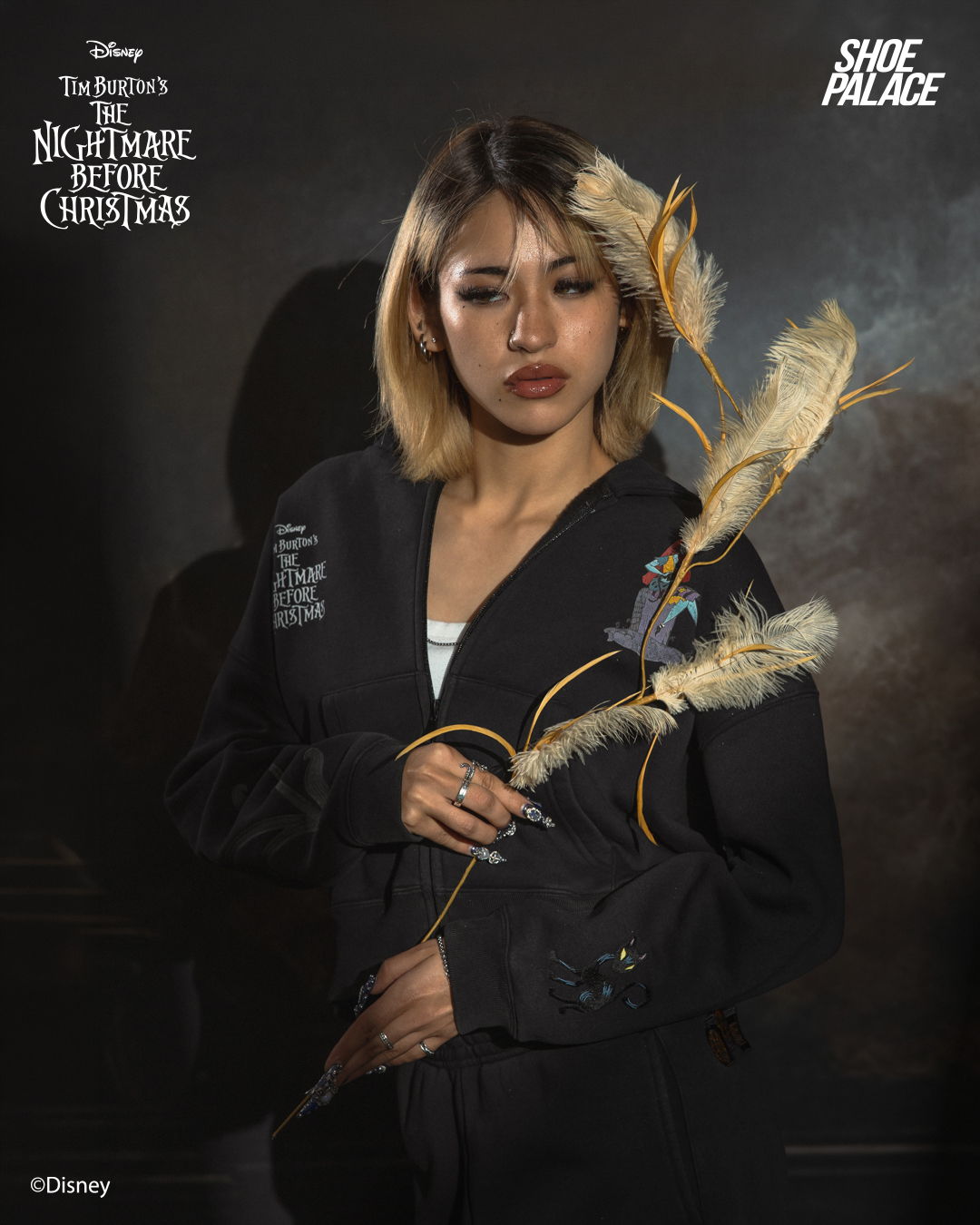 A person holding a decorative branch, dressed in dark attire against a moody background.