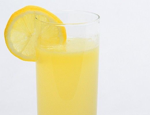 A glass of yellow lemonade with a lemon slice on the rim.