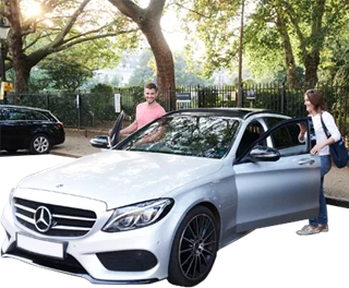 Two people interacting near a silver Mercedes car in a park setting