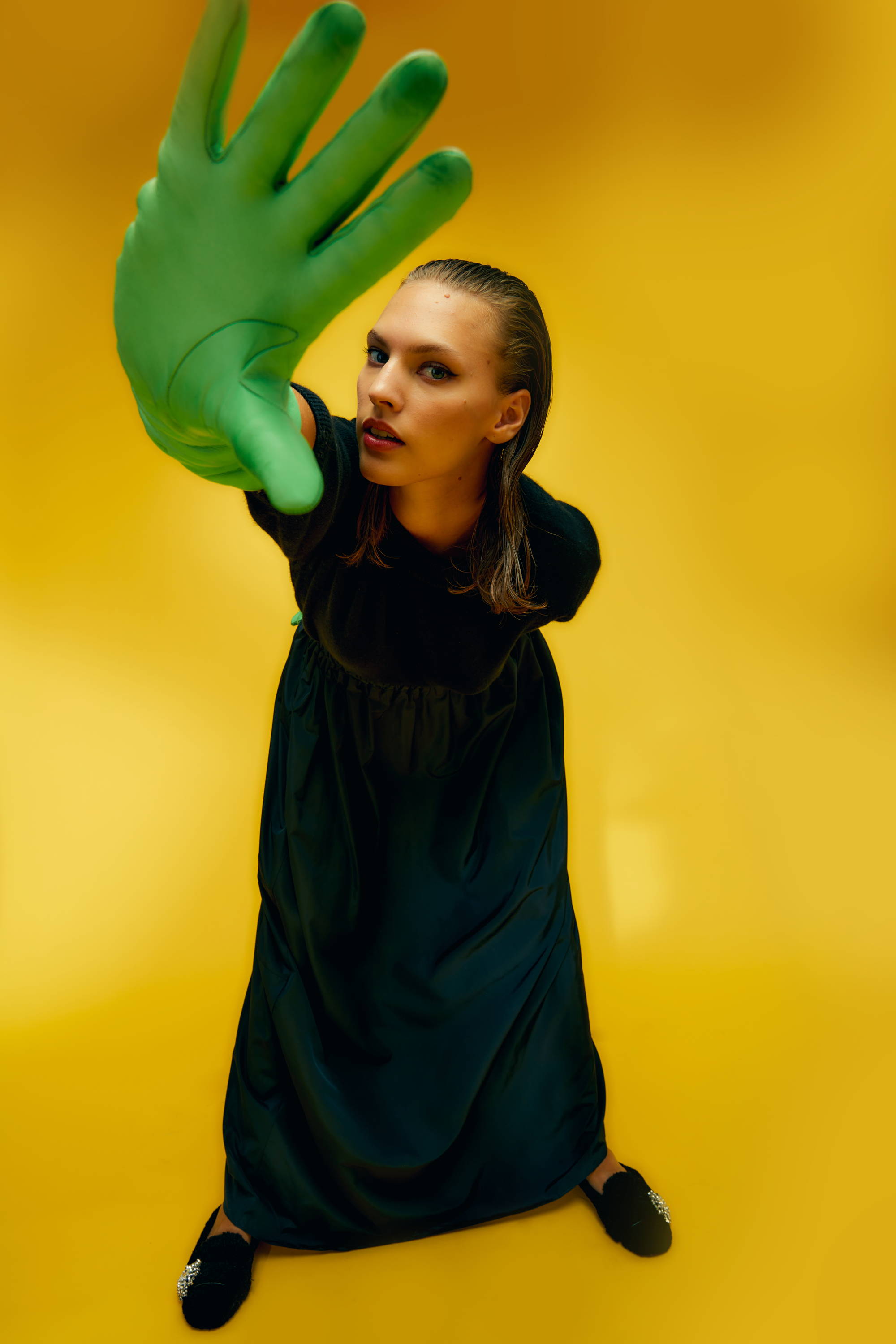 Person in a green glove poses against a yellow background.