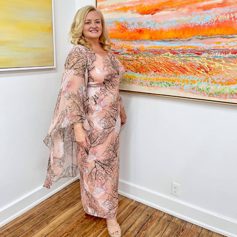 Camilla Webster wearing pink coral printed silk dress with attached capelet at her gallery by Ala von Auersperg