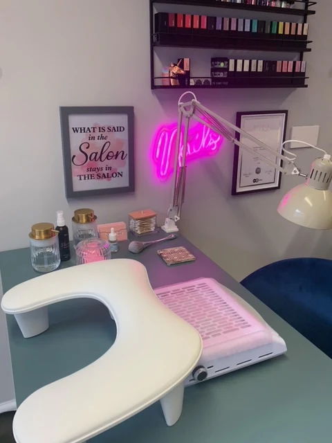 Nail salon workspace with equipment, neon sign, and colorful nail polish display.