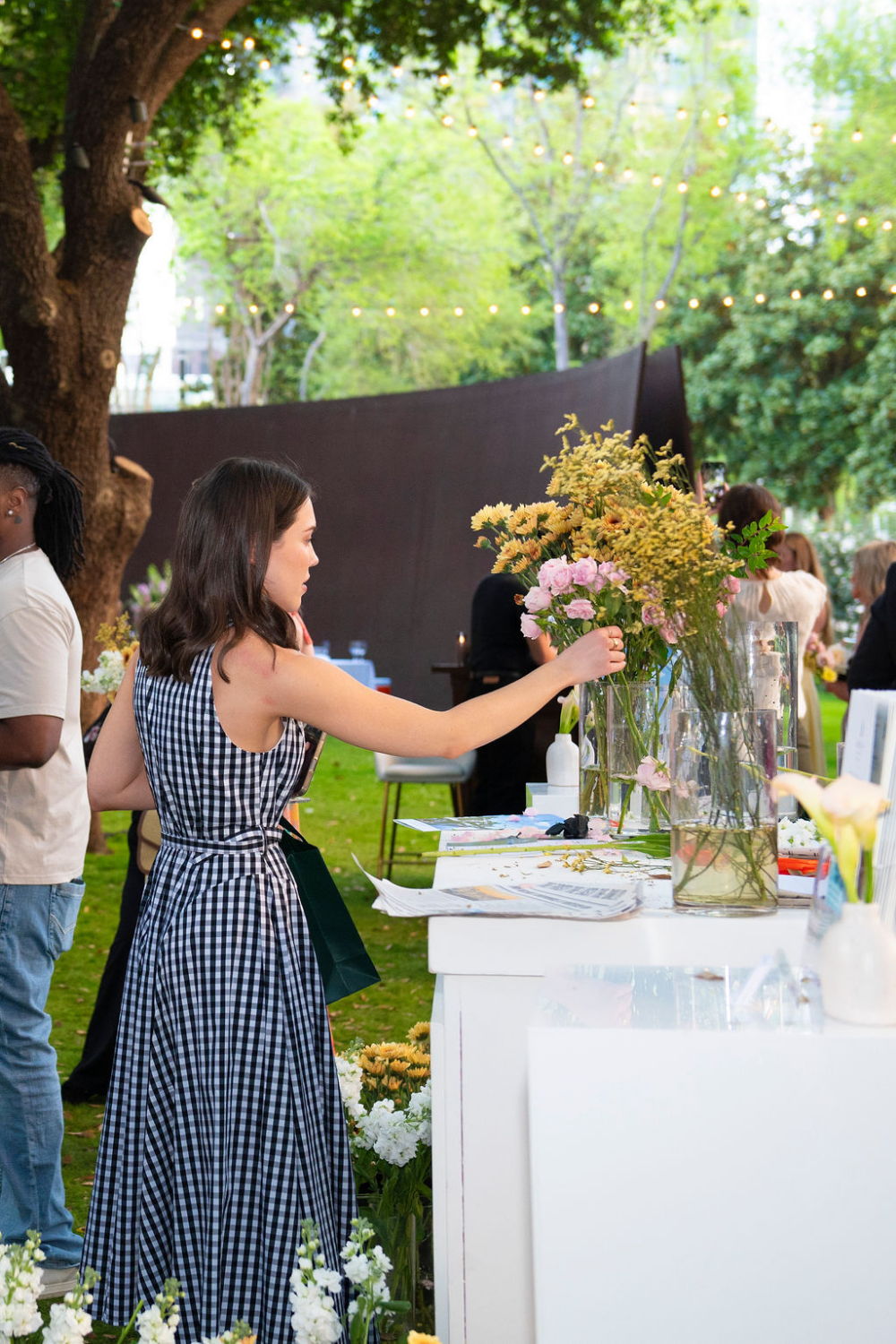 Woman arranging flowers at an outdoor event with greenery and decorations.