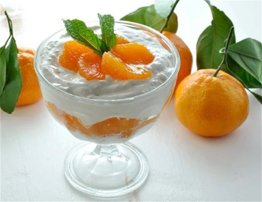 A glass dessert with cream, mandarin oranges, and mint leaves.